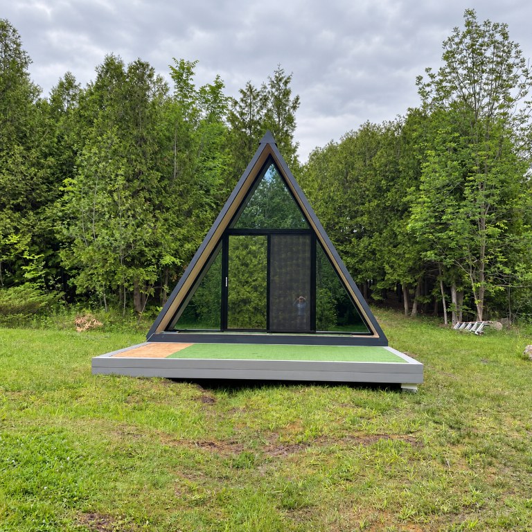 Finished CENLUXE A-Frame cabin with glazed sliding door, set on a grass site surrounded by trees